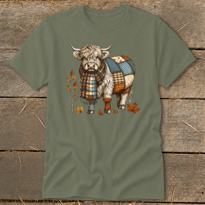 Fluffy cow wearing a patchwork blanket and plaid scarf, surrounded by autumn leaves.