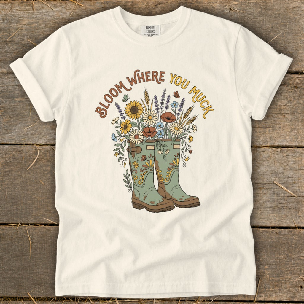 White t-shirt with green boots and a bouquet of flowers with "Bloom Where You Muck" text.