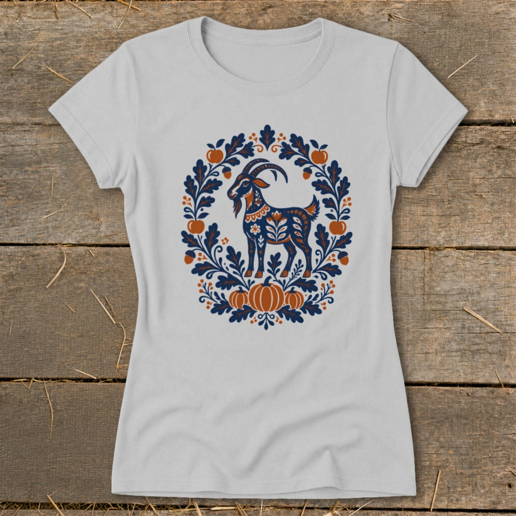 A light gray short-sleeve t-shirt features a folk-art graphic of a goat framed by leaves, apples, and pumpkins.