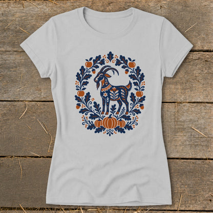 A light gray short-sleeve t-shirt features a folk-art graphic of a goat framed by leaves, apples, and pumpkins.