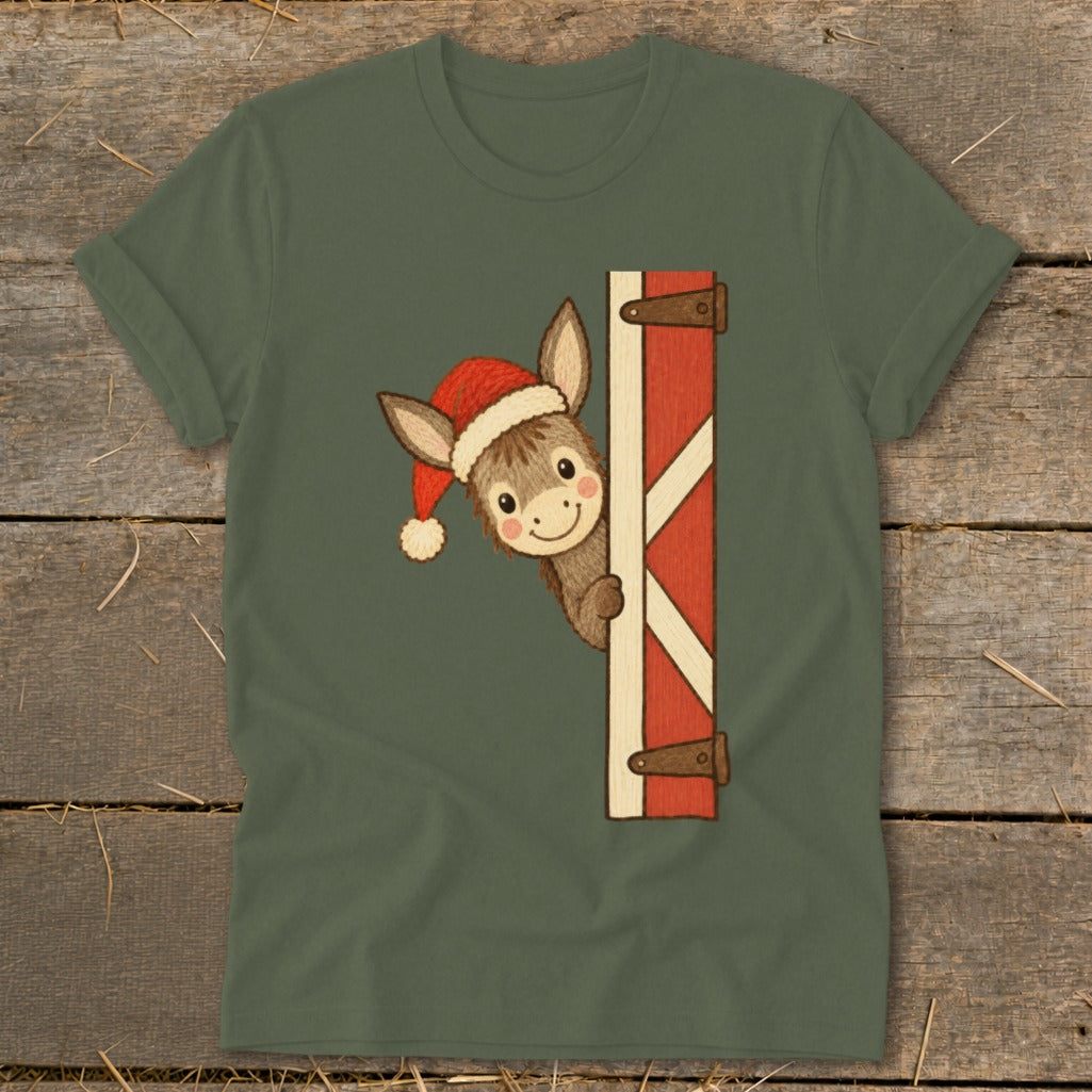 Donkey peeking from barn door wearing a Santa hat on a green t-shirt.
