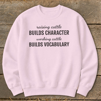 Pink sweatshirt with black text: "raising cattle BUILDS CHARACTER, working cattle BUILDS VOCABULARY".
