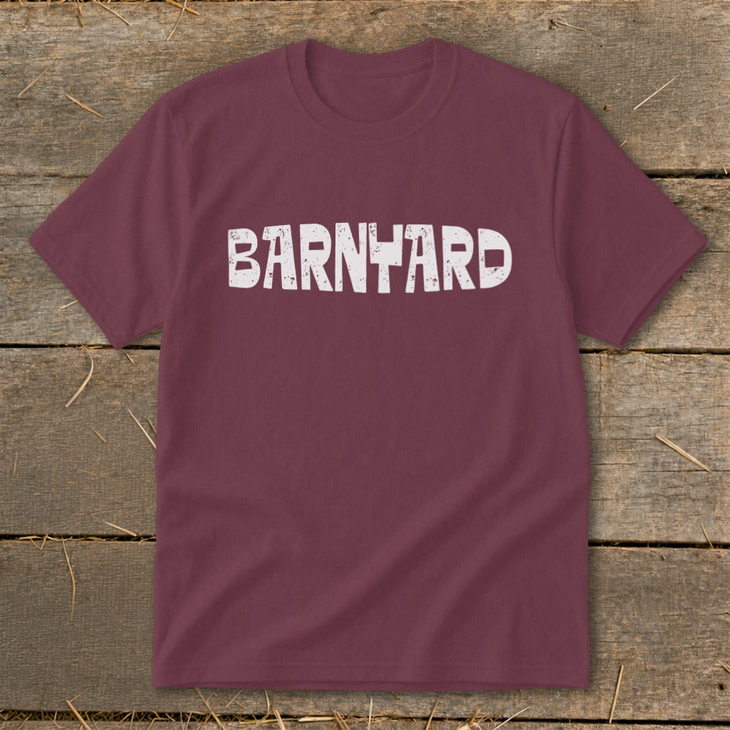 A maroon crewneck t-shirt featuring the distressed white text BARNYARD centered on the chest, laid flat on a rustic wooden background.