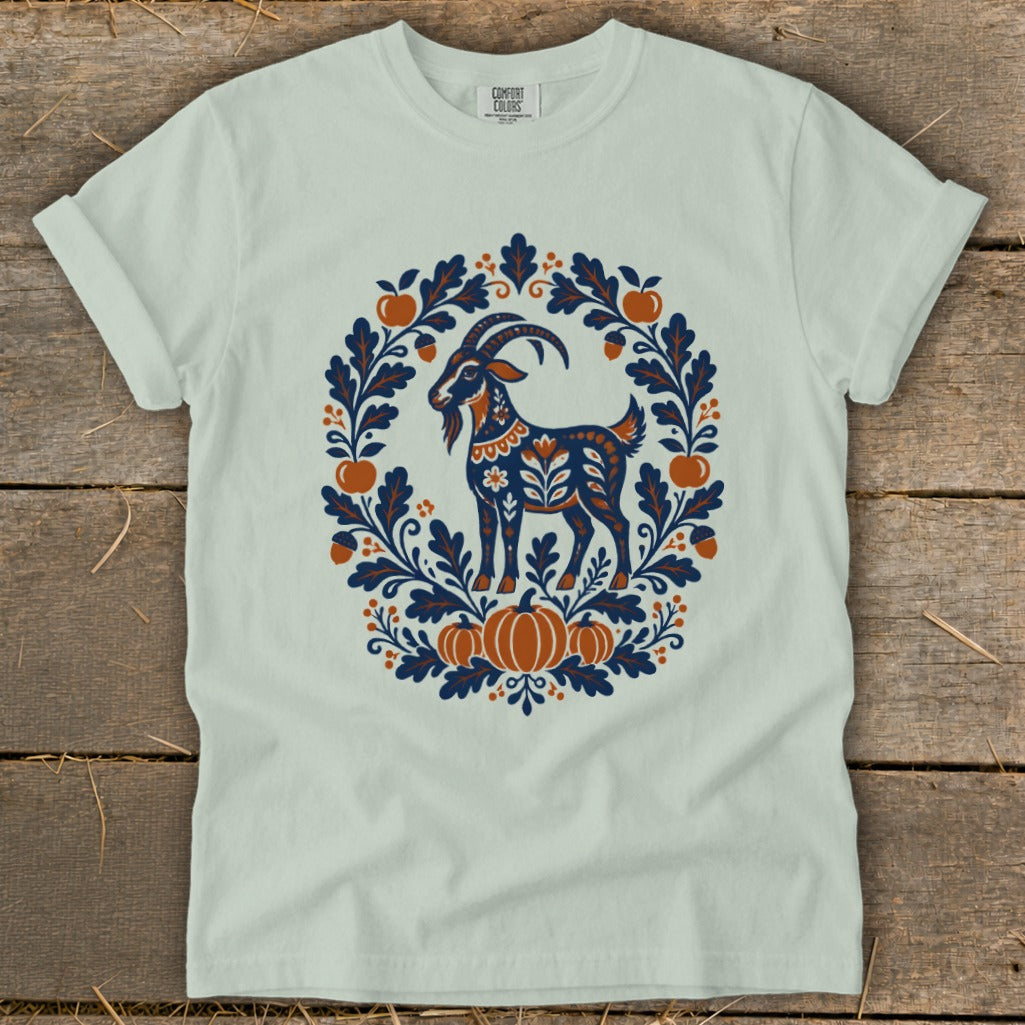 Sage green t-shirt featuring a folk art graphic of a goat surrounded by autumn foliage and pumpkins.