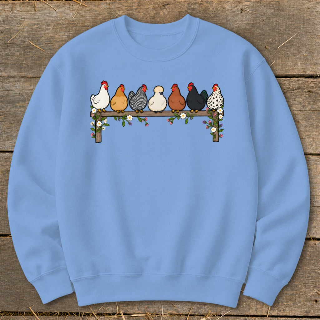 Light blue crewneck sweatshirt featuring a center graphic of seven colorful chickens perched on a flower-covered wooden fence.