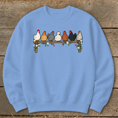 Light blue crewneck sweatshirt featuring a center graphic of seven colorful chickens perched on a flower-covered wooden fence.