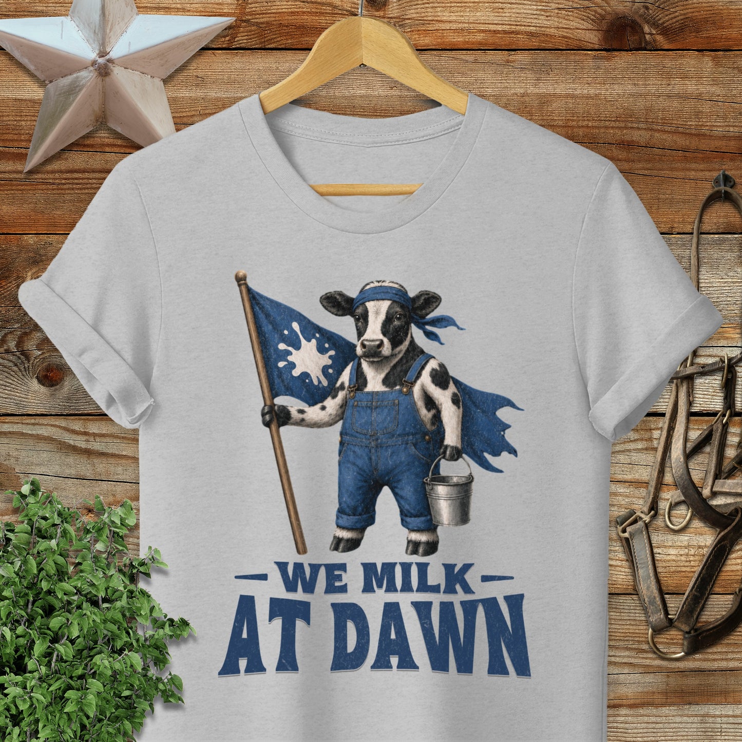 Cow in overalls holding flag with "We Milk At Dawn" text.