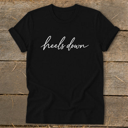 Black t-shirt with white "heels down" script text.