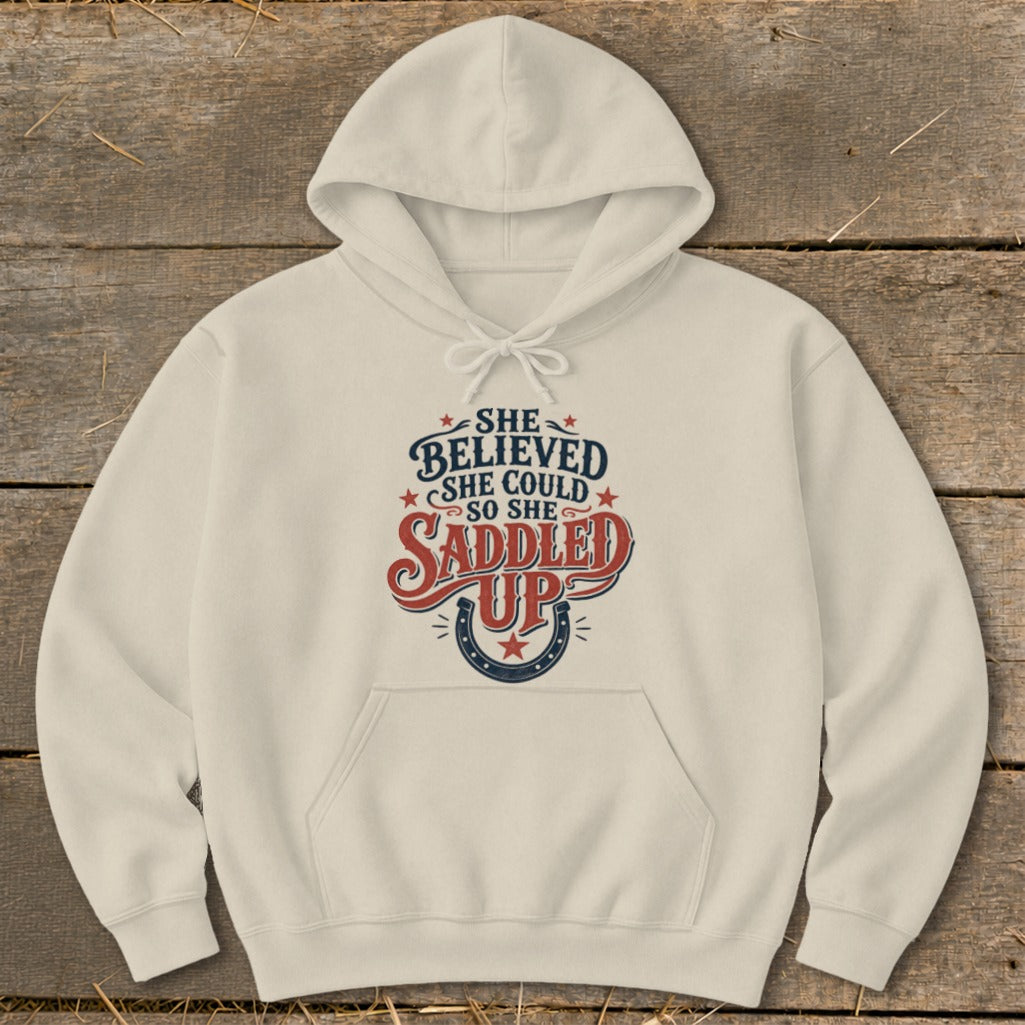 Cream hoodie with "She believed she could so she saddled up" text and horseshoe graphic.