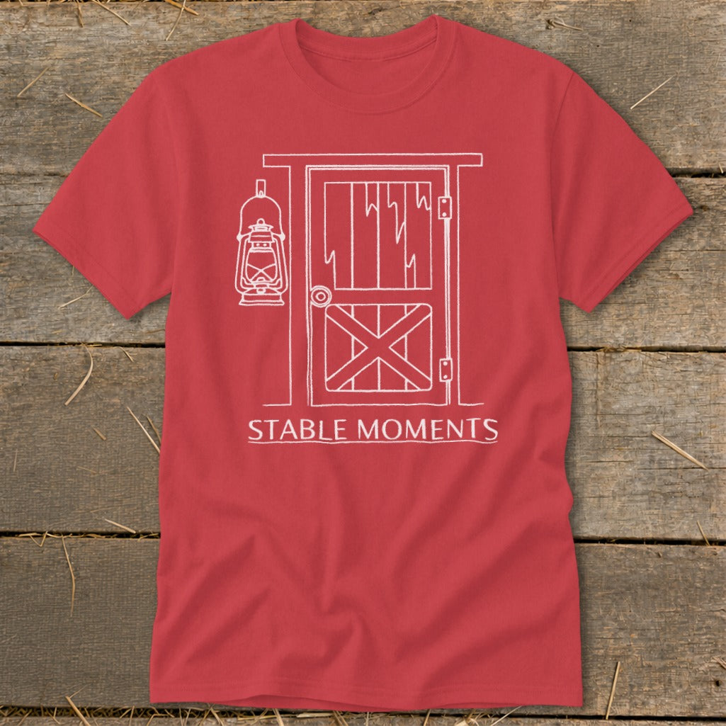 Red t-shirt with white line art of a barn door, lantern, and text "STABLE MOMENTS".