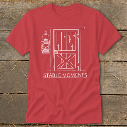 Red t-shirt with white line art of a barn door, lantern, and text "STABLE MOMENTS".
