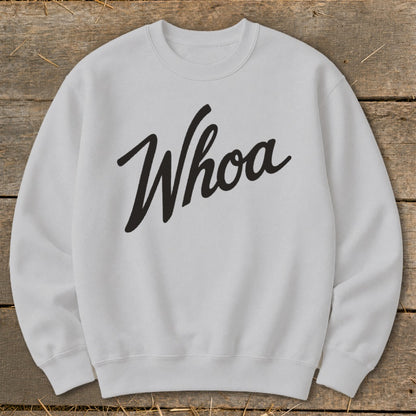 Grey crewneck sweatshirt with black "Whoa" text on a wooden background.
