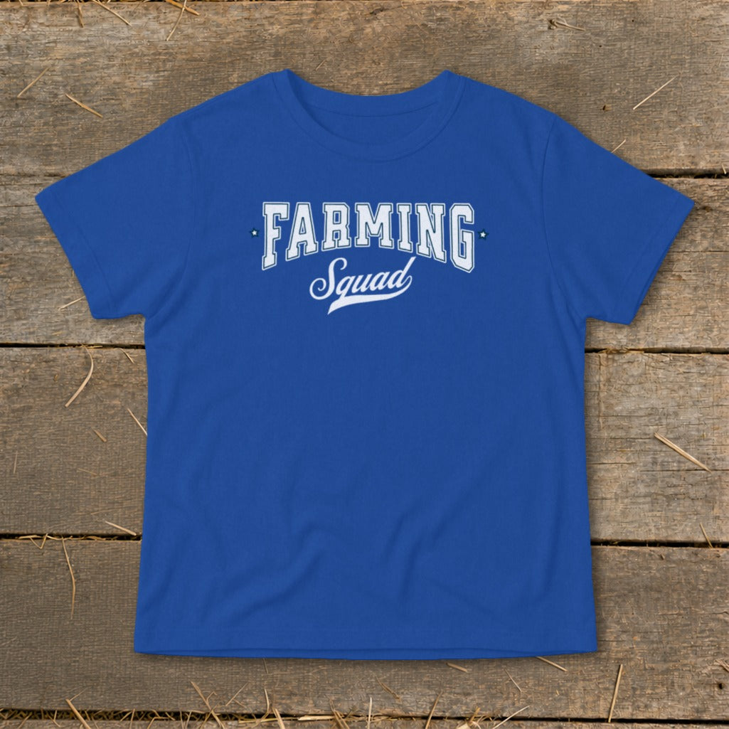 Royal blue t-shirt with white "Farming Squad" text and stars on a wooden background.