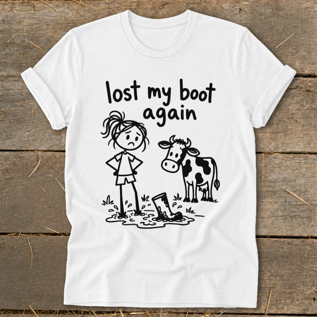 White t-shirt with a black graphic of a sad stick figure standing in mud next to a cow, with the text "lost my boot again".