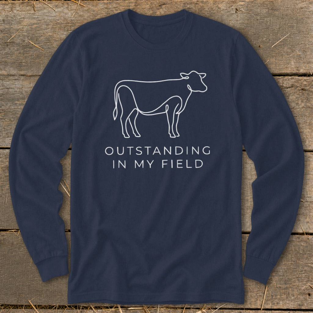 Navy long sleeve shirt with a white outline of a cow and the text "OUTSTANDING IN MY FIELD".