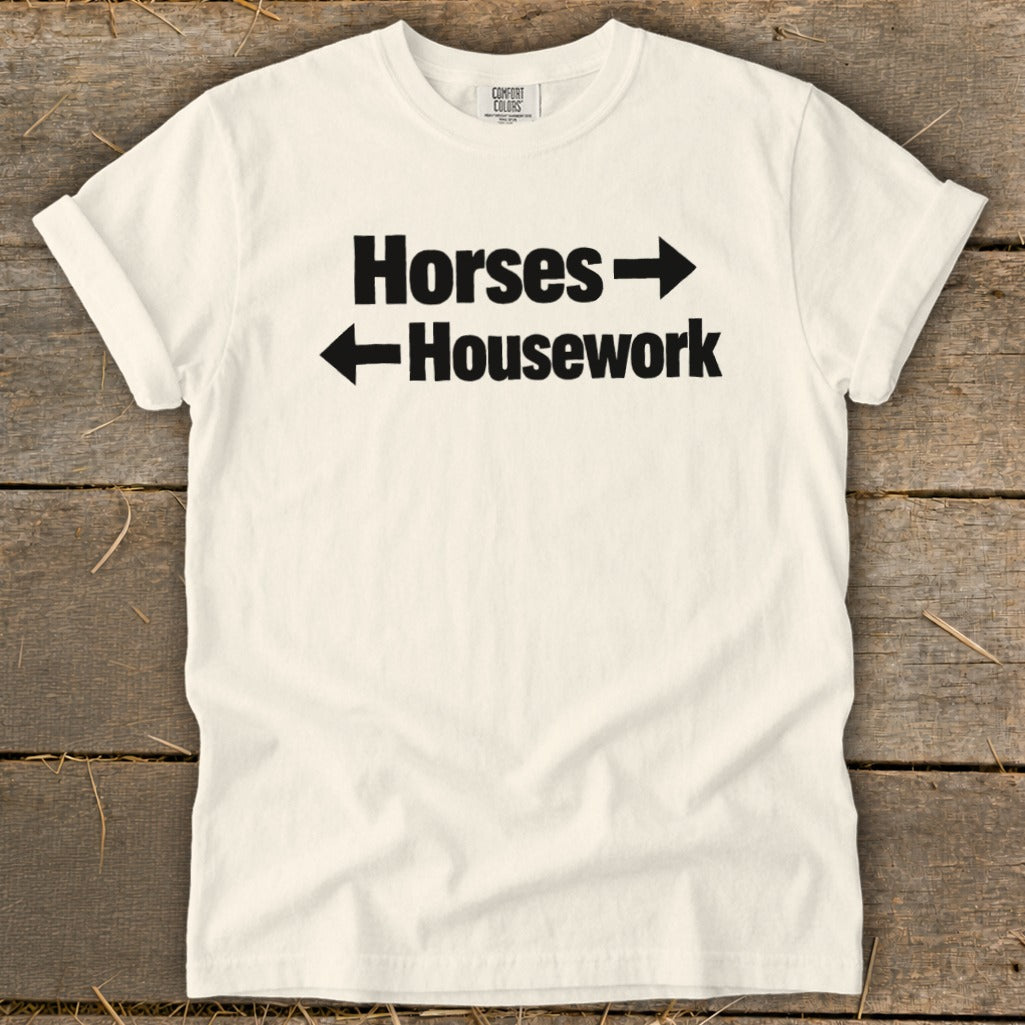 A white crewneck t-shirt with black text reading Horses with a right arrow above Housework with a left arrow.