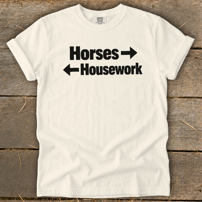 A white crewneck t-shirt with black text reading Horses with a right arrow above Housework with a left arrow.