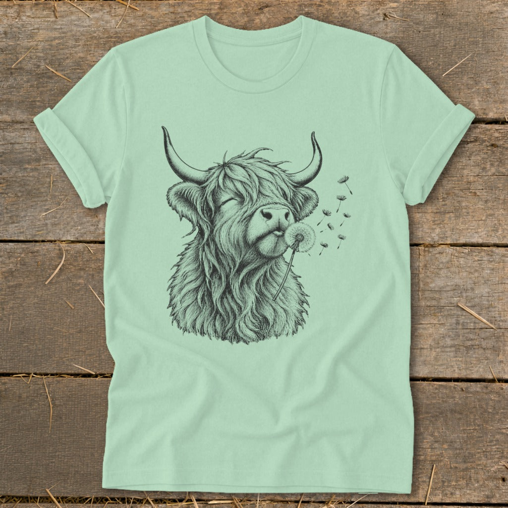 Light green t-shirt with a black sketch of a Highland cow blowing dandelion seeds.