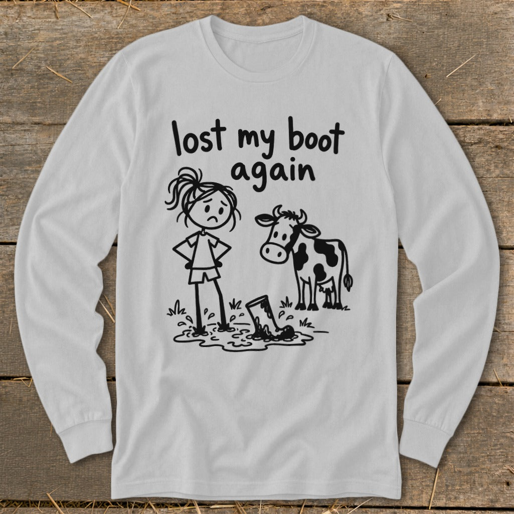 Light gray long-sleeve t-shirt with a humorous black line drawing of a girl, a cow, and a boot stuck in mud, accompanied by the text lost my boot again.