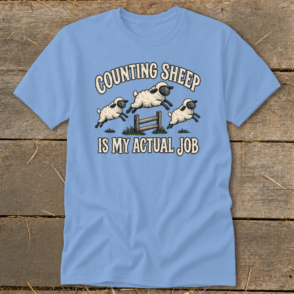 Light blue t-shirt with cartoon sheep jumping over a fence, reading "Counting Sheep Is My Actual Job".