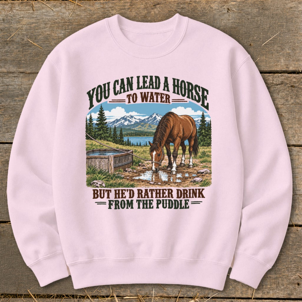Light pink crewneck sweatshirt featuring a graphic of a horse drinking from a puddle with mountain text.