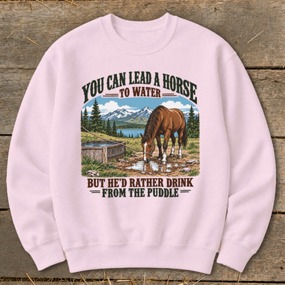 Light pink crewneck sweatshirt featuring a graphic of a horse drinking from a puddle with mountain text.
