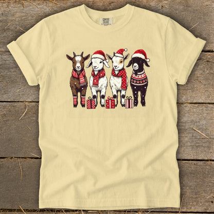 Four goats in festive attire stand with presents on a light yellow t-shirt.