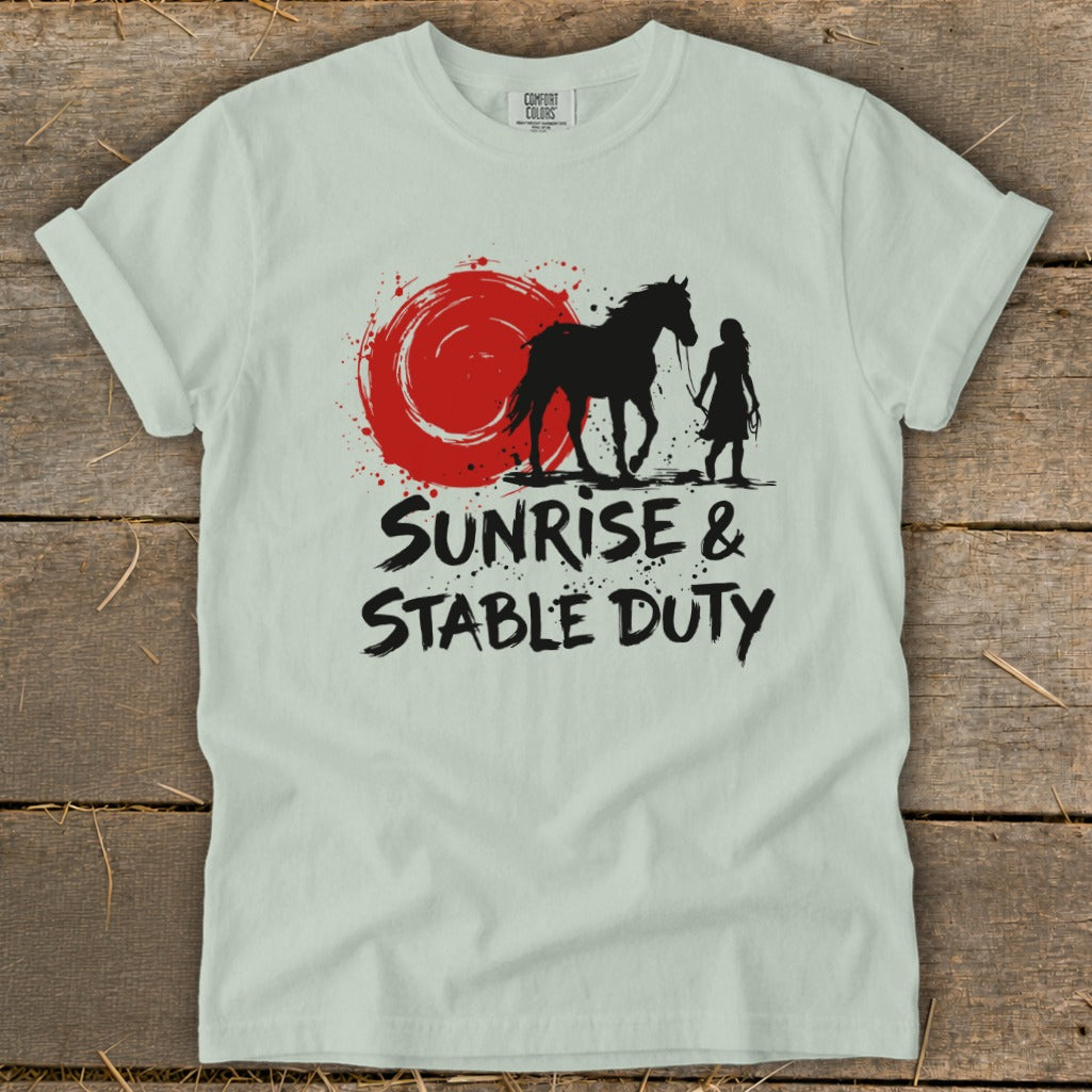 Light green t-shirt with black silhouette of a horse and rider beside a red sun graphic, text reads "Sunrise & Stable Duty."