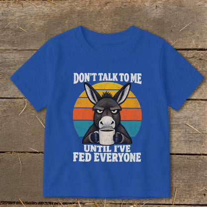 Royal blue t-shirt featuring an illustration of an annoyed donkey holding a coffee mug, overlaid on a sunset graphic with text reading "Don't Talk To Me Until I've Fed Everyone".