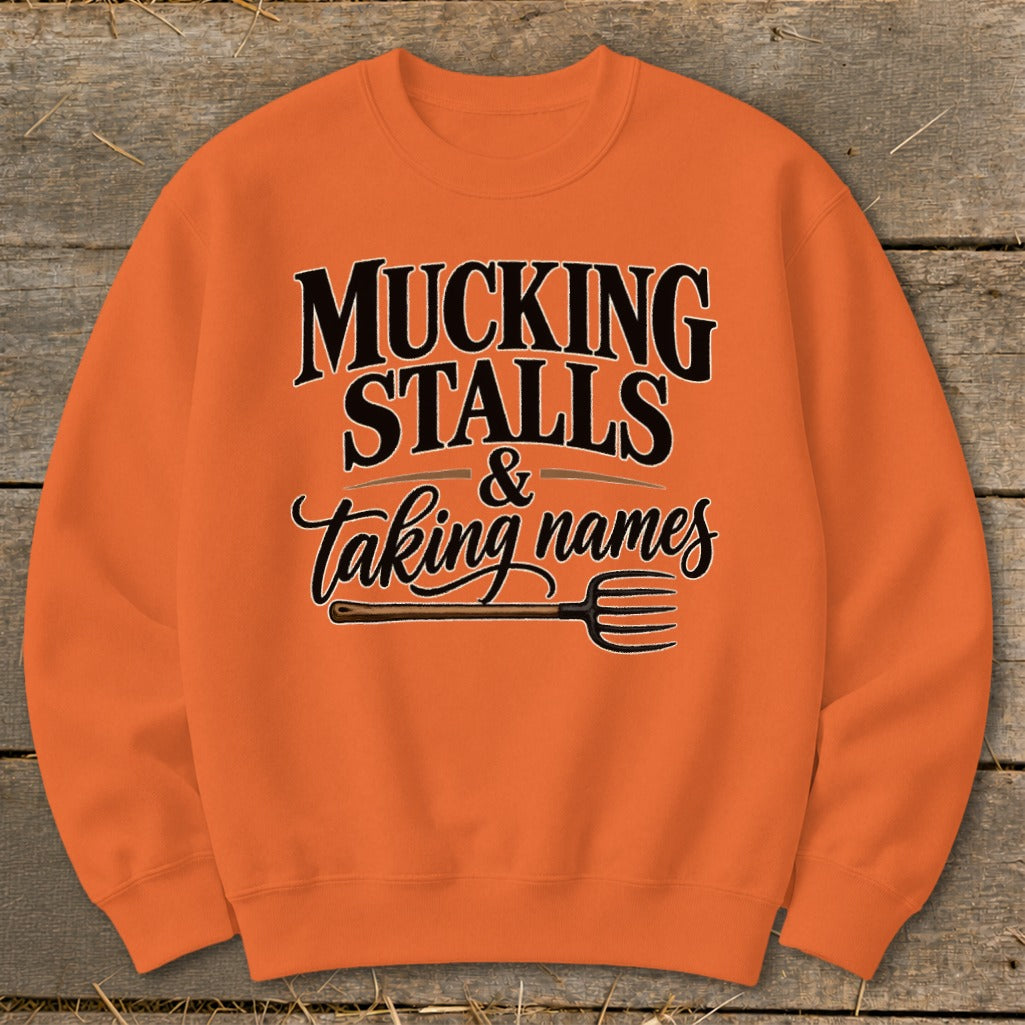Orange sweatshirt with text "Mucking Stalls & Taking Names" and a pitchfork graphic.