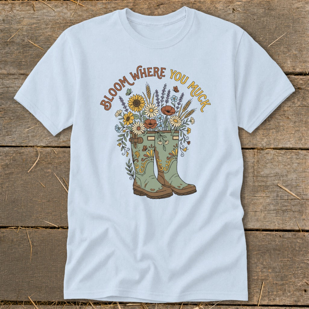 Light blue t-shirt with green boots and floral design, text says "Bloom Where You Muck".