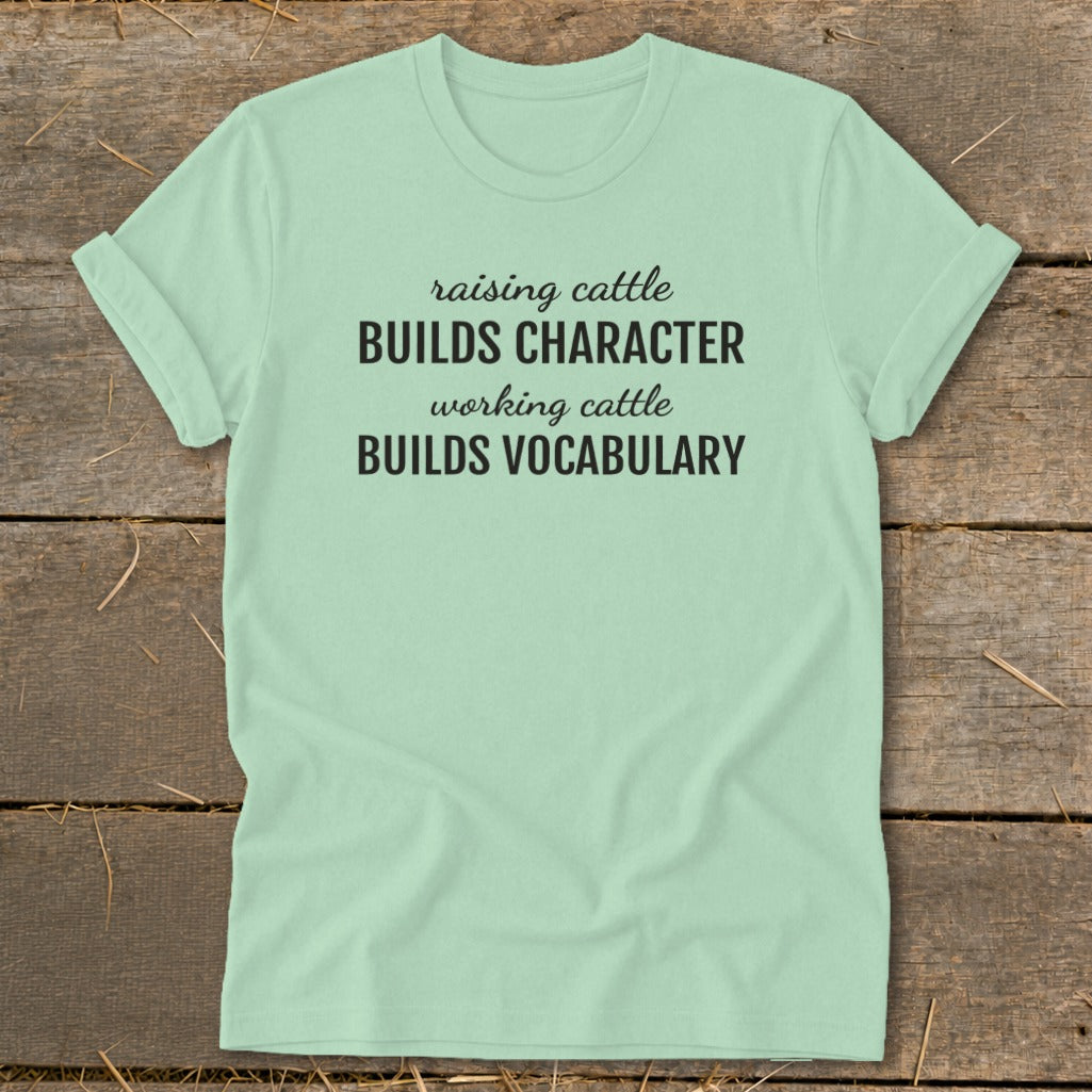 Light mint t-shirt with black text: "raising cattle BUILDS CHARACTER working cattle BUILDS VOCABULARY".