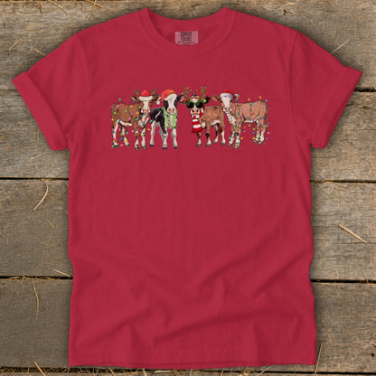 Five cartoon cows in Santa hats and Christmas lights stand in a line.