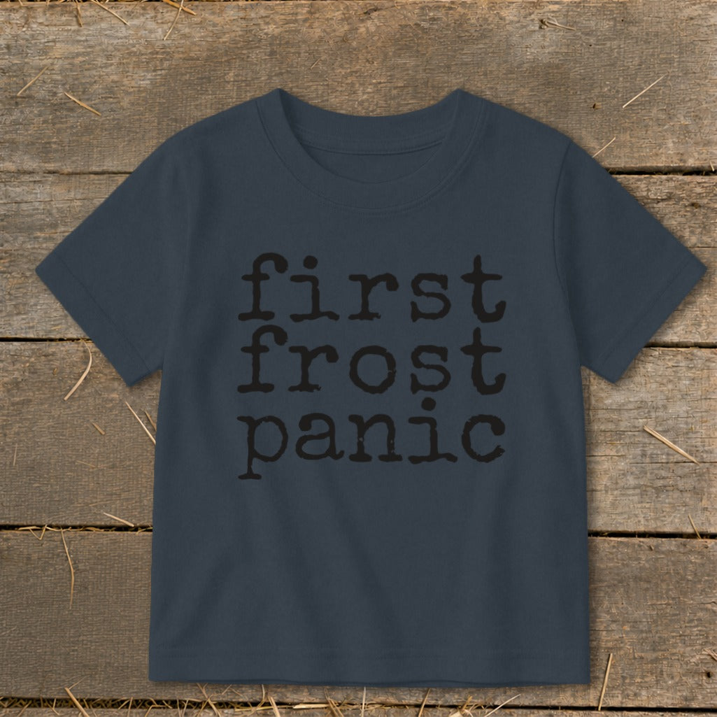 Navy t-shirt with black text "first frost panic" on a wooden background.