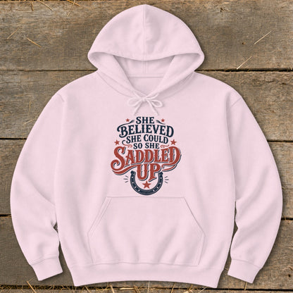 Pink hoodie with "She believed she could so she saddled up" text and horseshoe graphic.