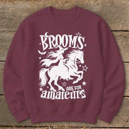 Maroon sweatshirt with white graphic: witch riding horse, "BROOMS ARE FOR AMATEURS" text.