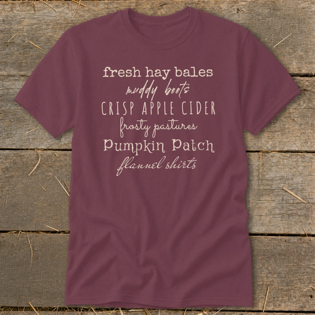 Burgundy t-shirt with white text listing "fresh hay bales, muddy boots, crisp apple cider, frosty pastures, pumpkin patch, flannel shirts."