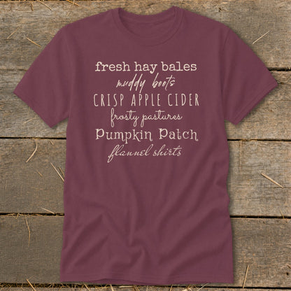 Burgundy t-shirt with white text listing "fresh hay bales, muddy boots, crisp apple cider, frosty pastures, pumpkin patch, flannel shirts."