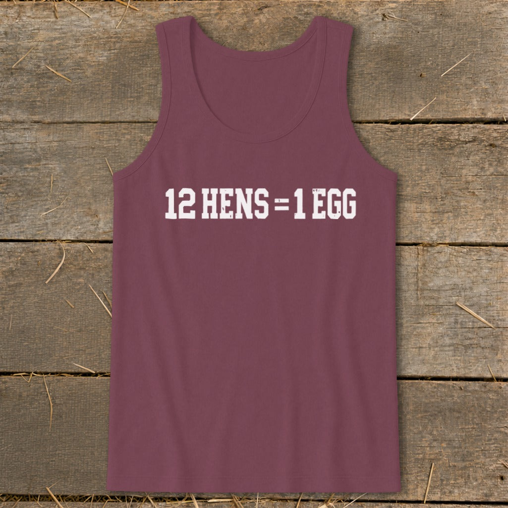 A maroon tank top with white text that reads 12 HENS = 1 EGG, laid flat on a rustic wooden background.