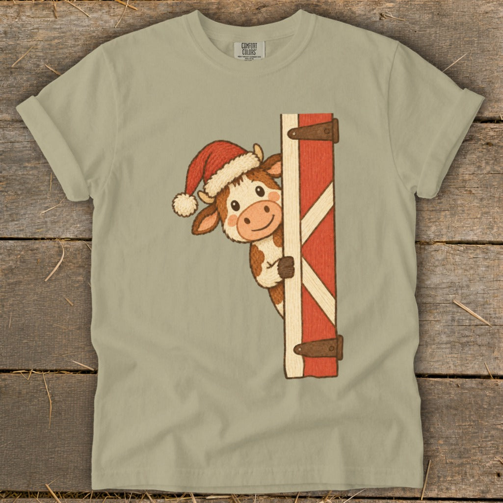 Cartoon cow wearing a Santa hat peeking from behind a barn door.