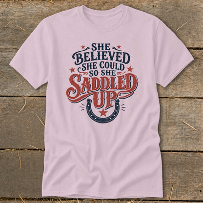 Pink t-shirt with "She Believed She Could So She Saddled Up" graphic and horseshoe.