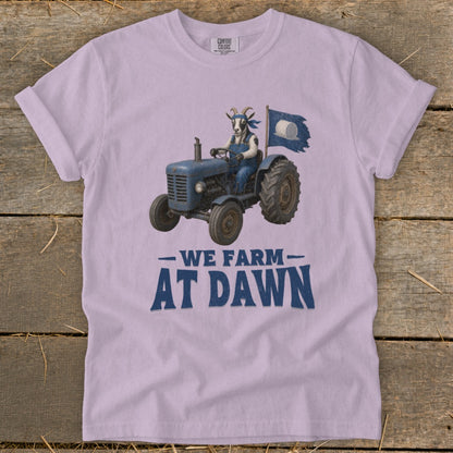 Goat in overalls driving a blue tractor with a "We Farm At Dawn" slogan.