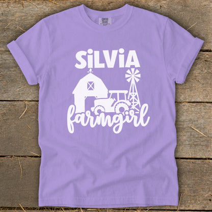 Purple t-shirt with white graphic of "SILVIA farmgirl" over barn, tractor, and windmill.