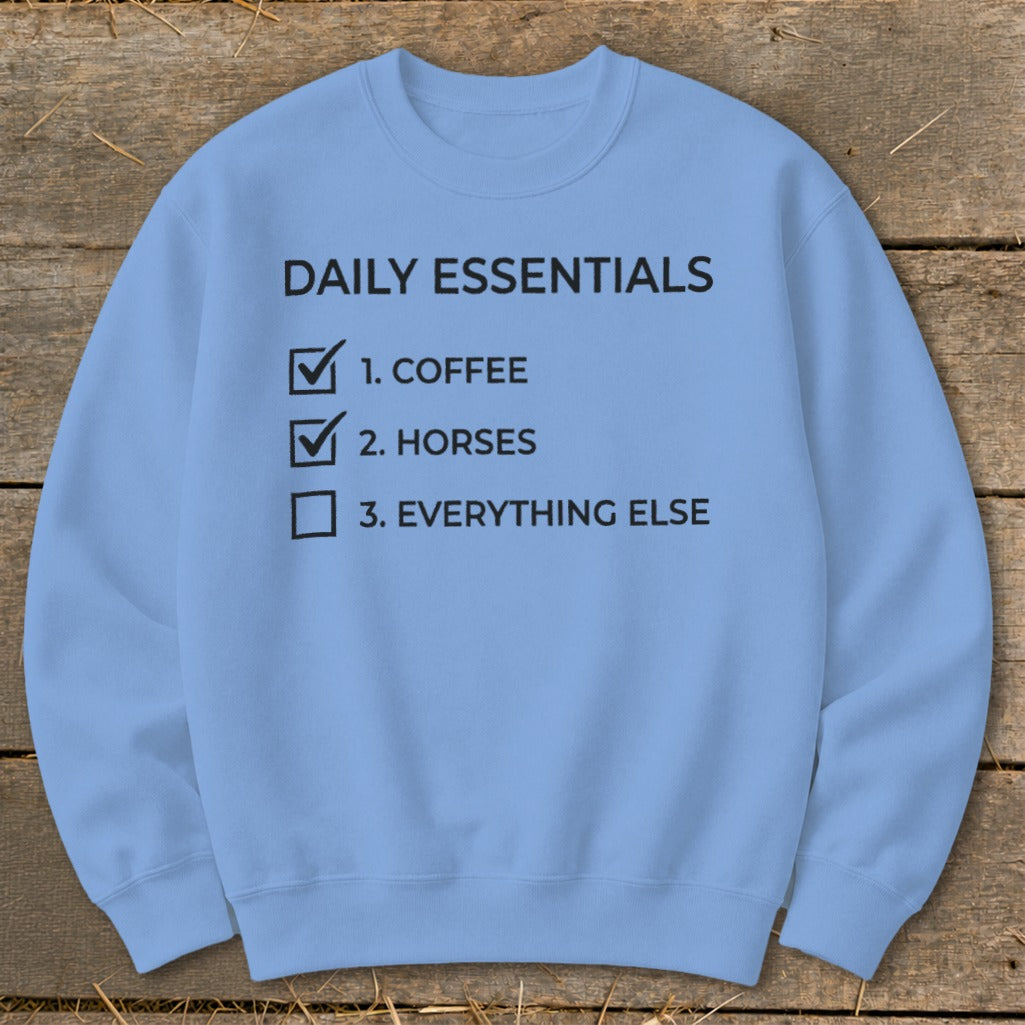Light blue sweatshirt with black text listing daily essentials: coffee and horses checked.