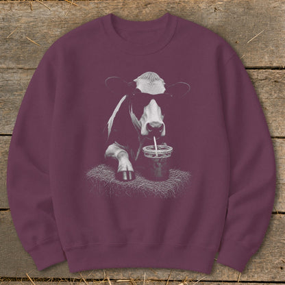 Black and white cow wearing sunglasses drinks from a cup on a maroon sweatshirt.