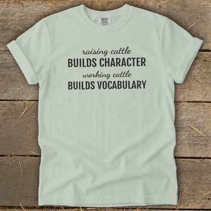Light blue t-shirt with text "raising cattle BUILDS CHARACTER working cattle BUILDS VOCABULARY".