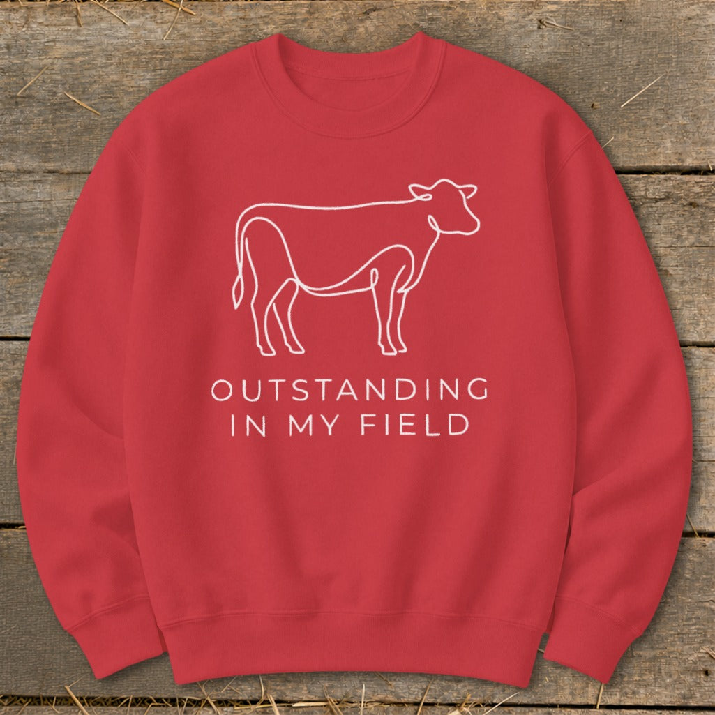 Red sweatshirt with a white outline of a cow and text "OUTSTANDING IN MY FIELD".