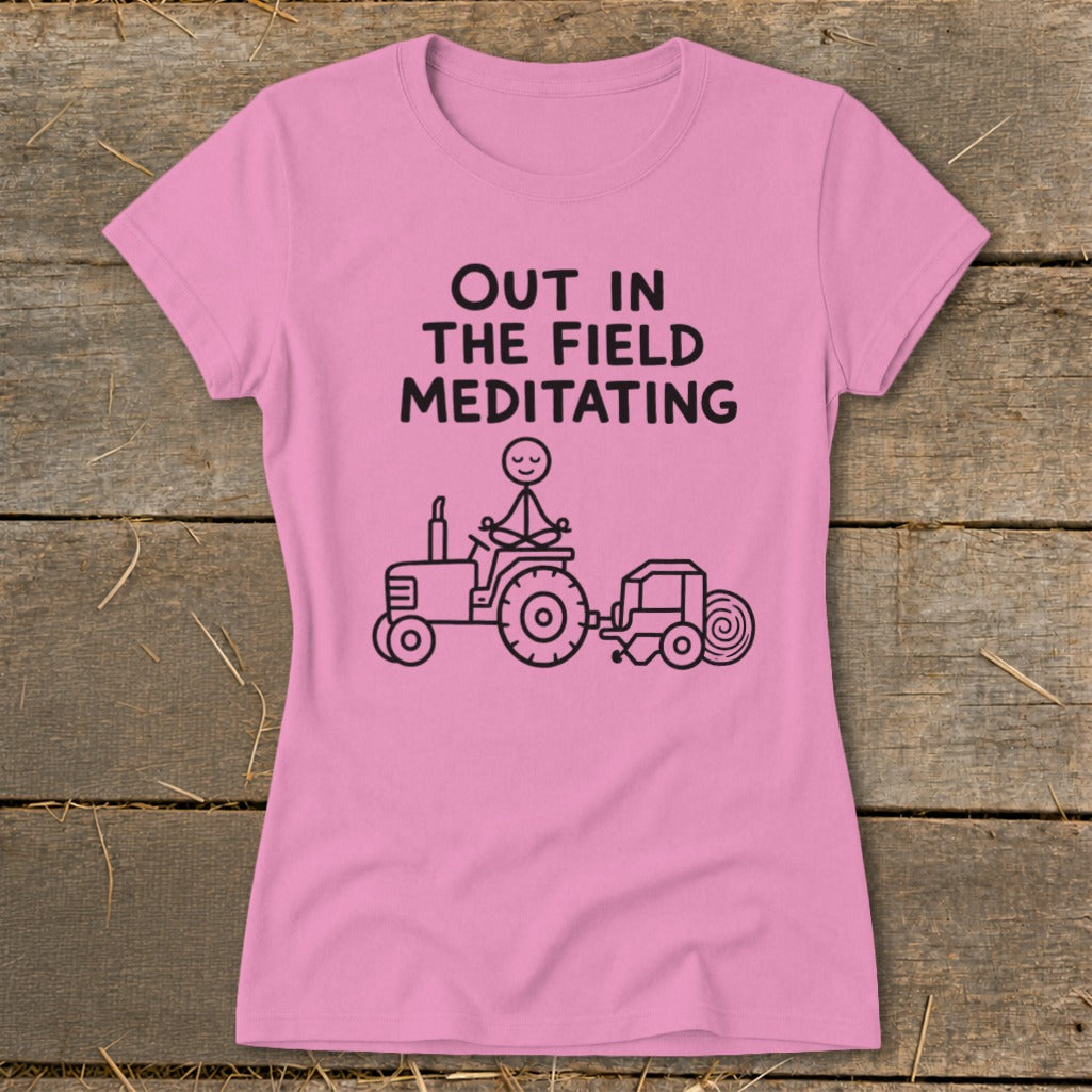 Pink t-shirt with "Out in the Field Meditating" text and drawing of stick figure meditating on a tractor.