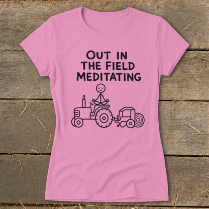 Pink t-shirt with "Out in the Field Meditating" text and drawing of stick figure meditating on a tractor.