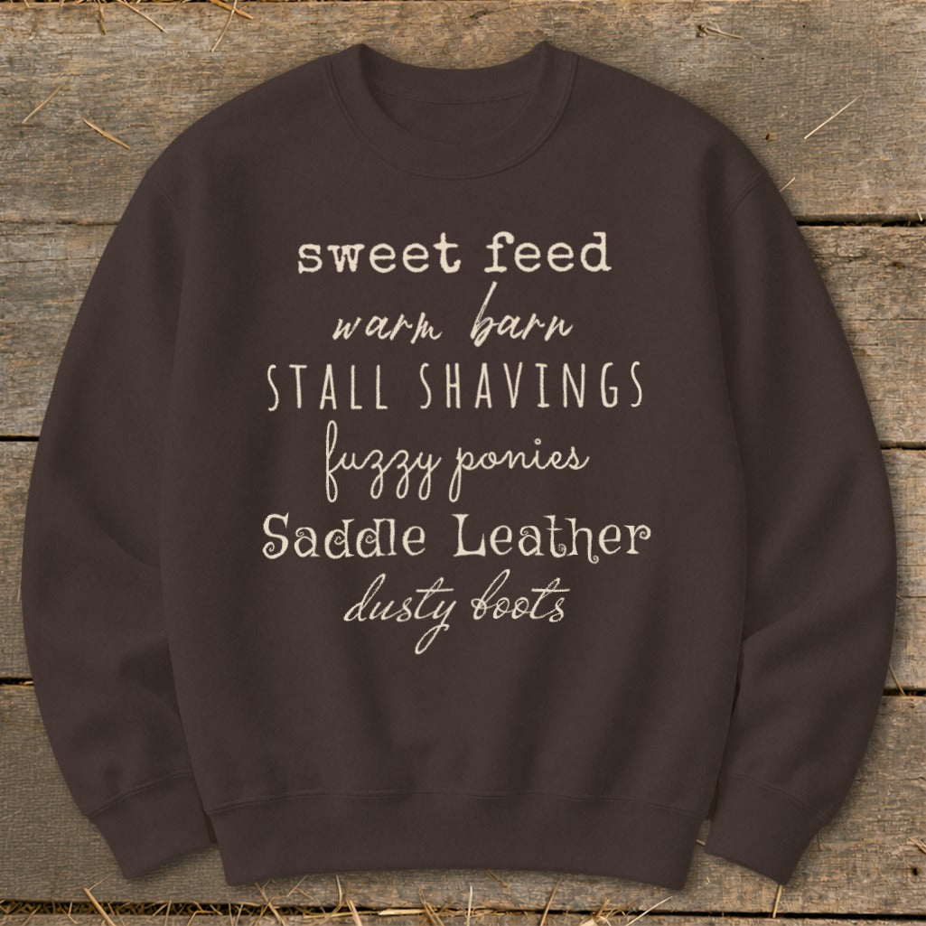 Brown sweatshirt with text listing "sweet feed, warm barn, stall shavings, fuzzy ponies, saddle leather, dusty boots".